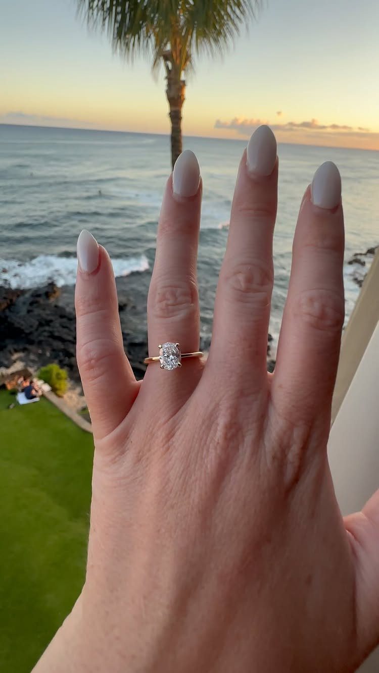 Diamond engagement ring on a hand with a tropical beach sunset background