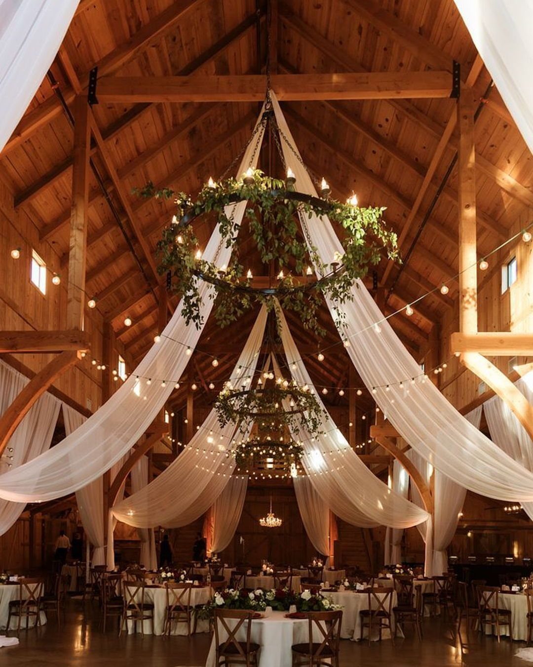 Rustic barn interior decorated with white fabric draping and greenery for a wedding.