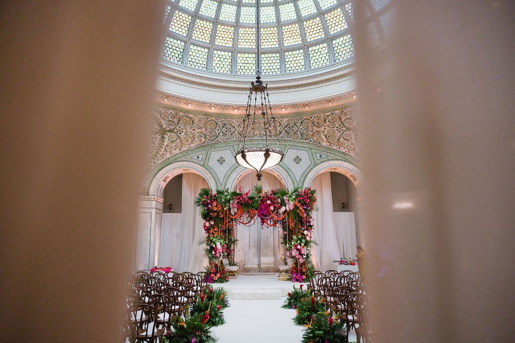 Wedding ceremony setup with floral arch under an ornate glass dome ceiling
