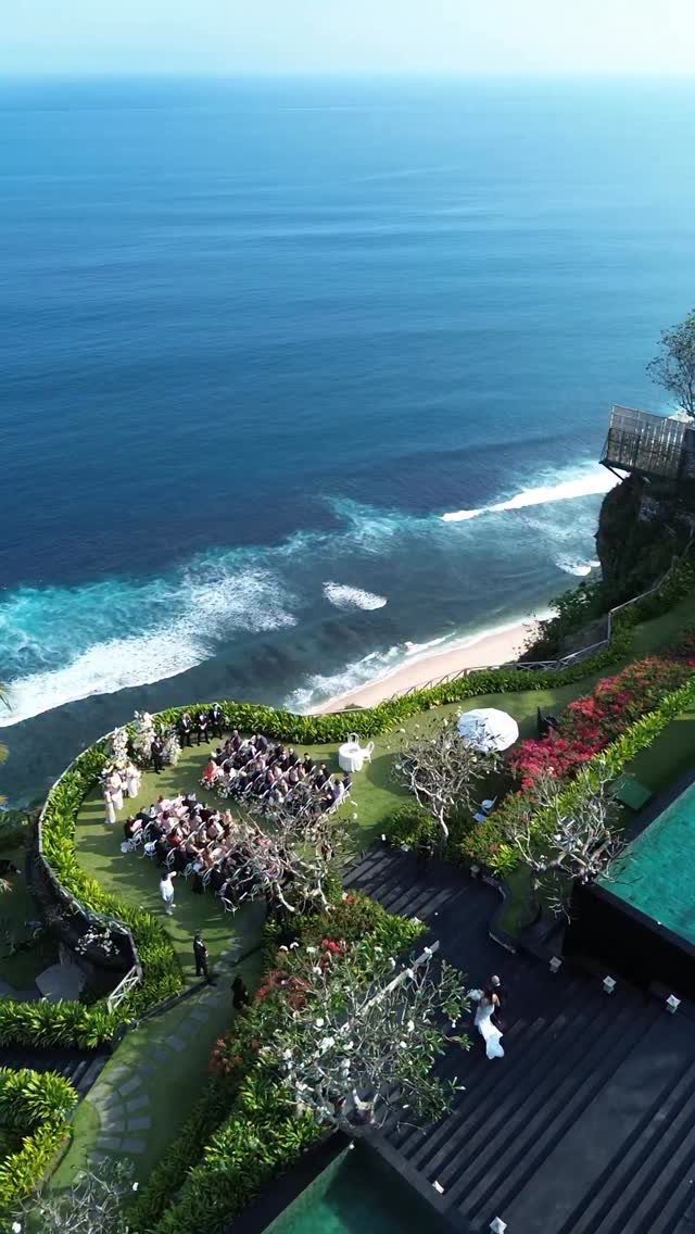 Wedding ceremony on a green cliffside overlooking a blue ocean and sandy beach