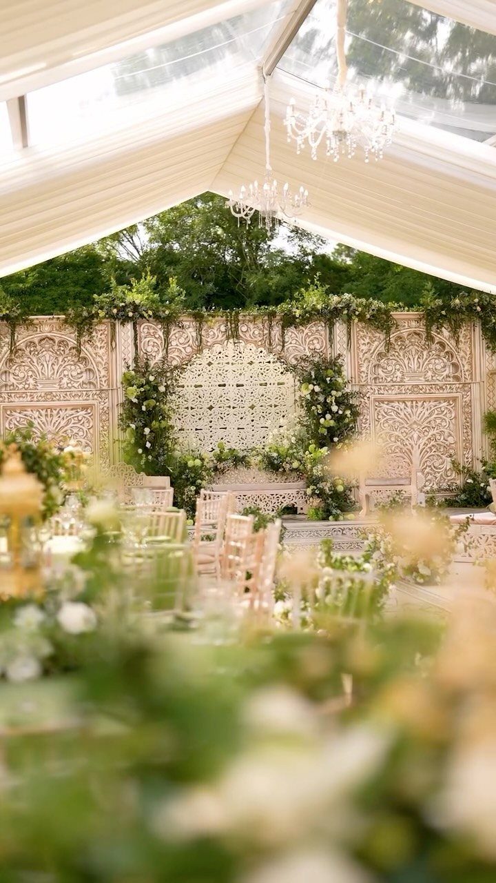 Wedding ceremony setup under a white tent with carved backdrop and chandeliers
