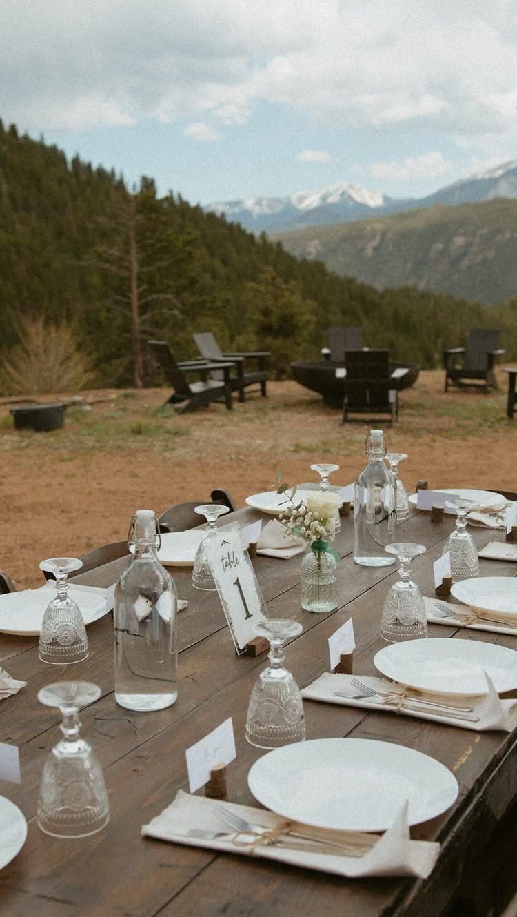 Wooden dining table set for a wedding overlooking a mountain valley and forest.