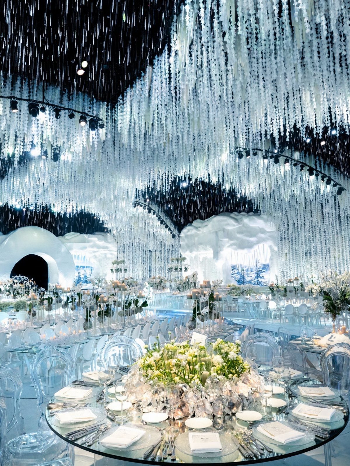 Winter themed event space with glass tables, clear chairs, and shimmering ceiling decorations.