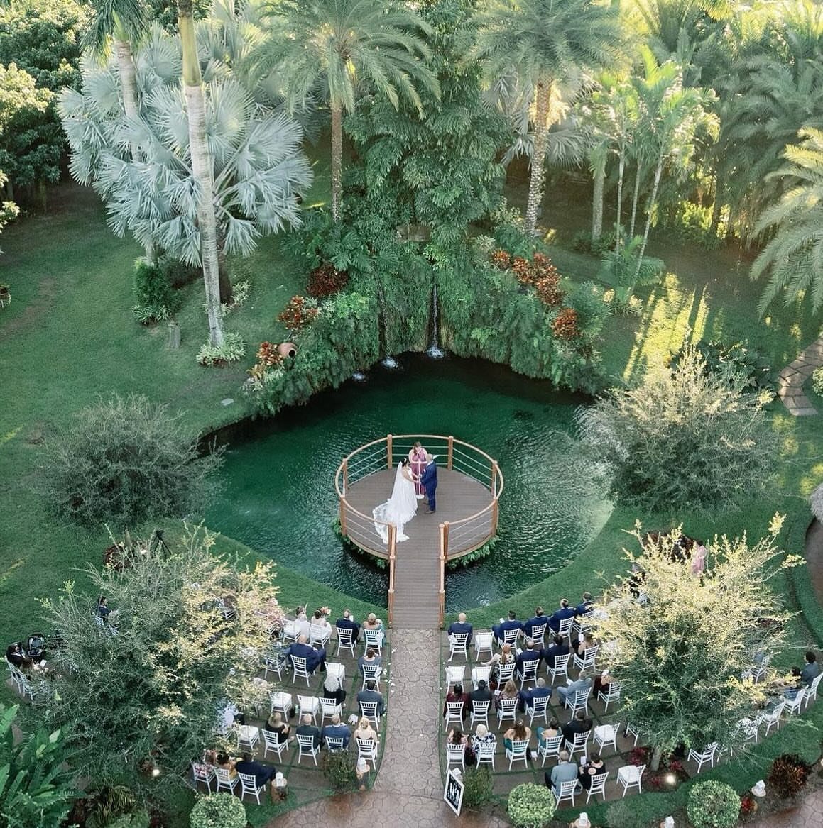 Wedding ceremony on a wooden deck over a pond surrounded by tropical palms.