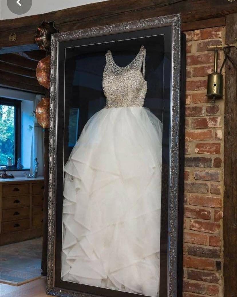 White wedding dress preserved and displayed inside a large silver framed glass case.