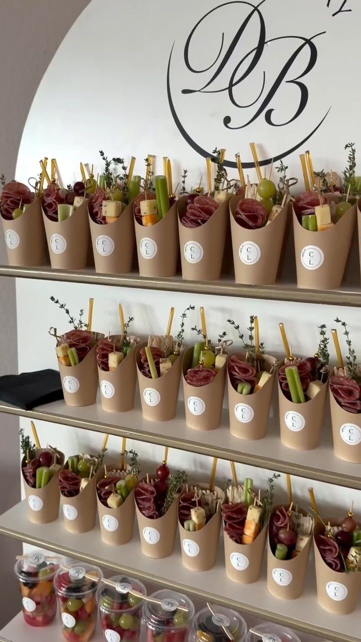 Charcuterie cones with meats and cheeses arranged on white shelves for a reception.