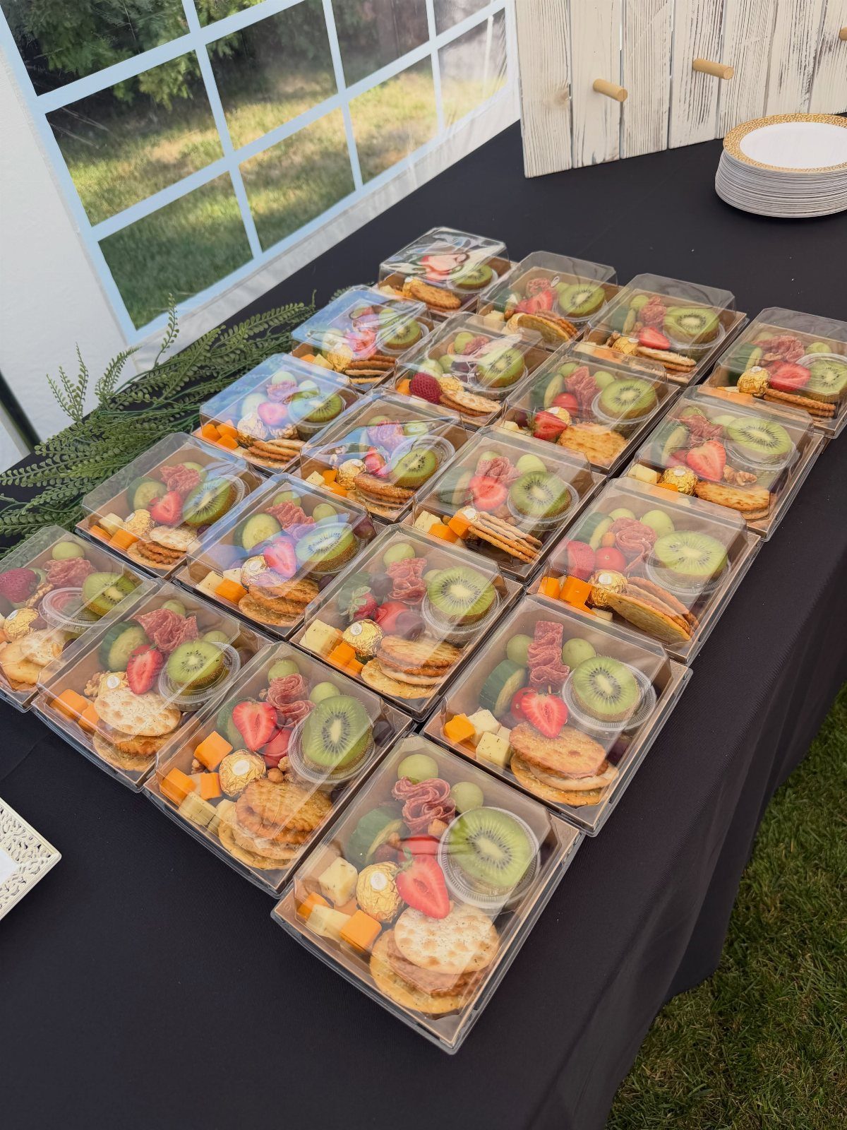 Charcuterie snack boxes with fruit and cheese arranged on a black table.