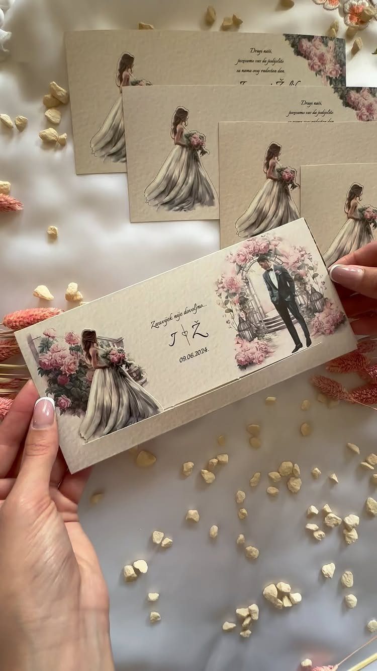Tan wedding invitations with bride and groom illustrations held by a person's hands.