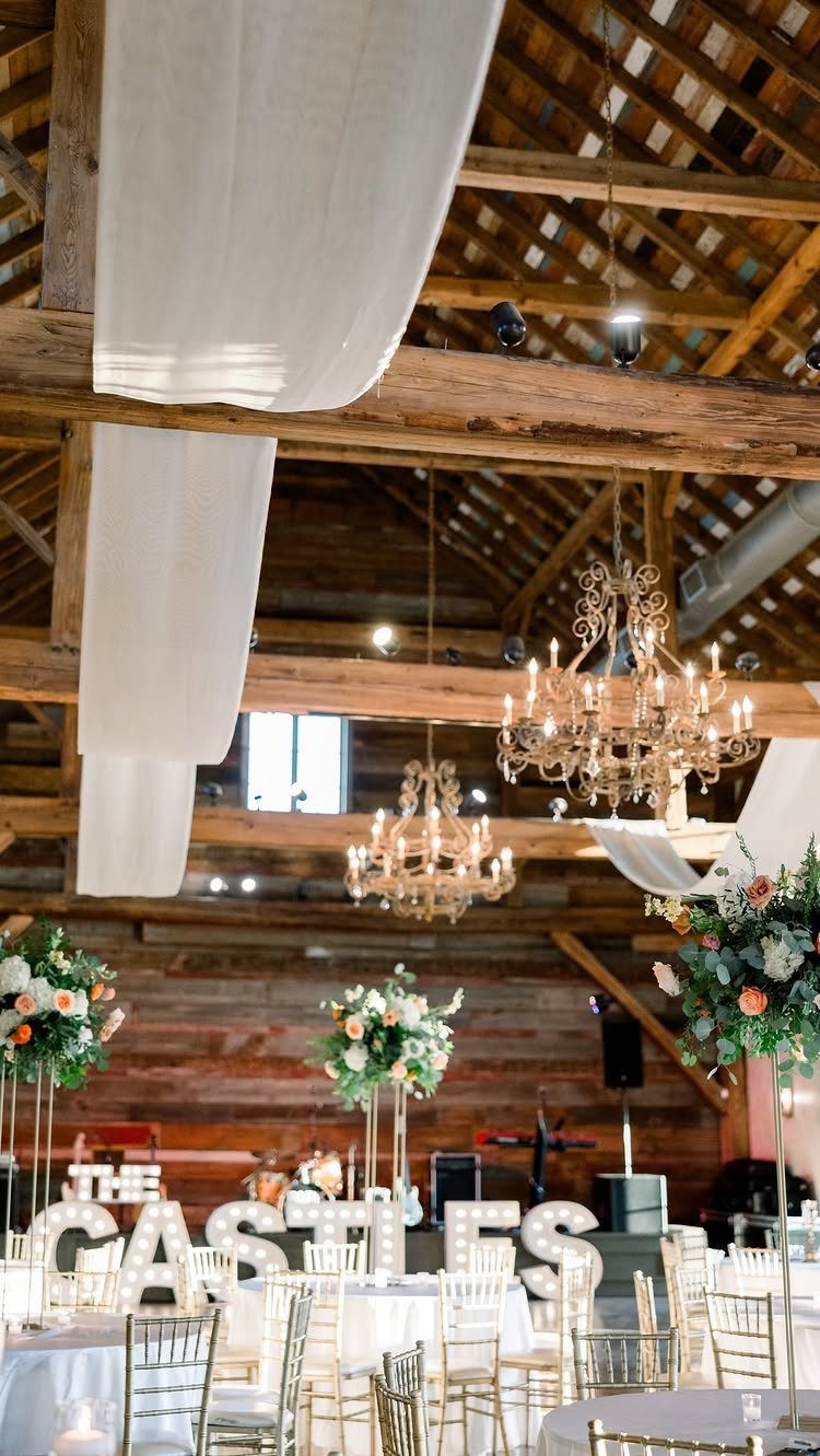Rustic barn wedding reception with chandeliers, white draping, and illuminated name letters.