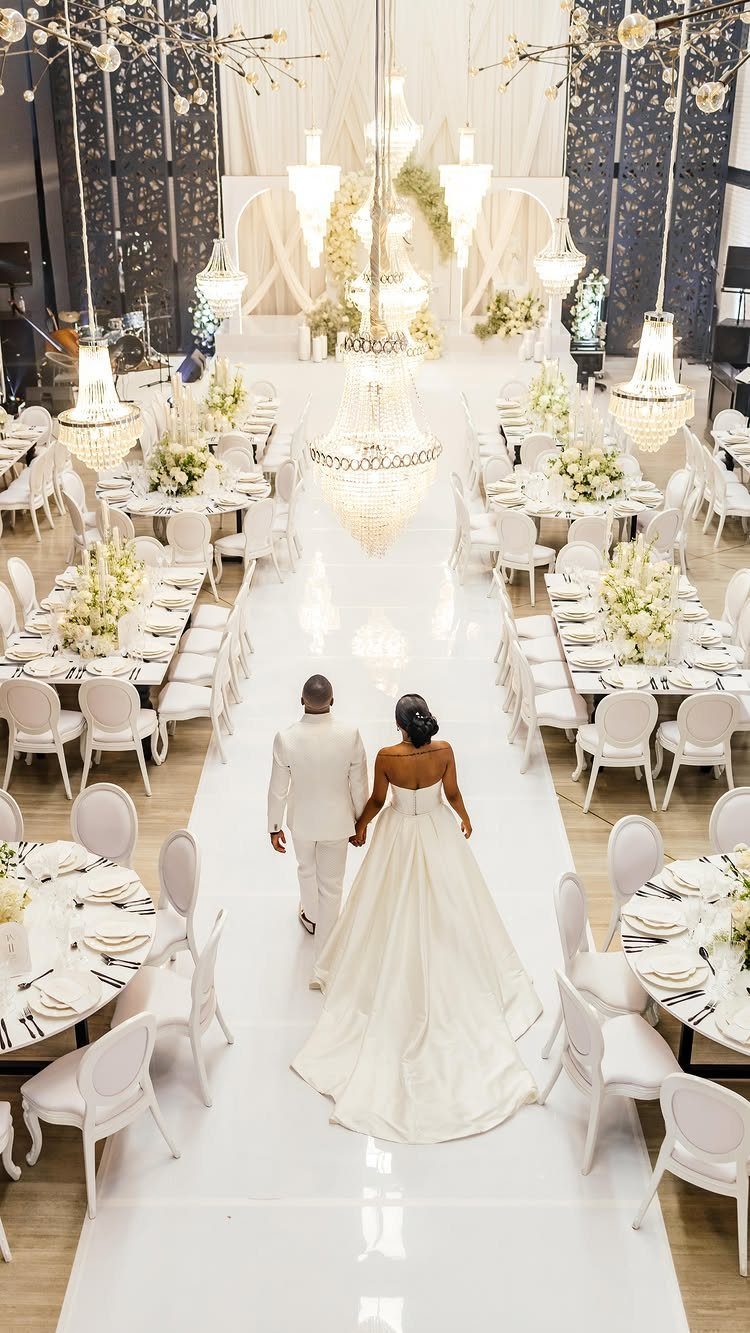 Bride and groom walking down a white aisle in a white decorated ballroom
