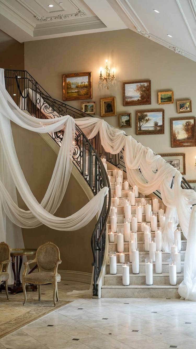 Grand staircase draped in white fabric with white pillar candles on marble steps