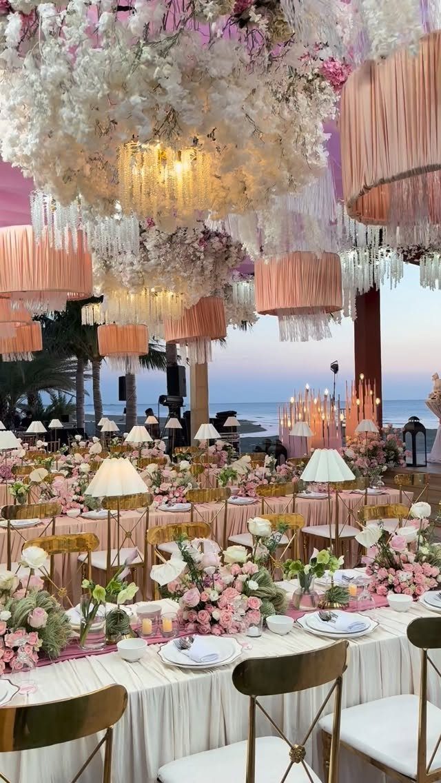 Opulent wedding reception tables with pink flowers and elaborate floral ceiling decorations.