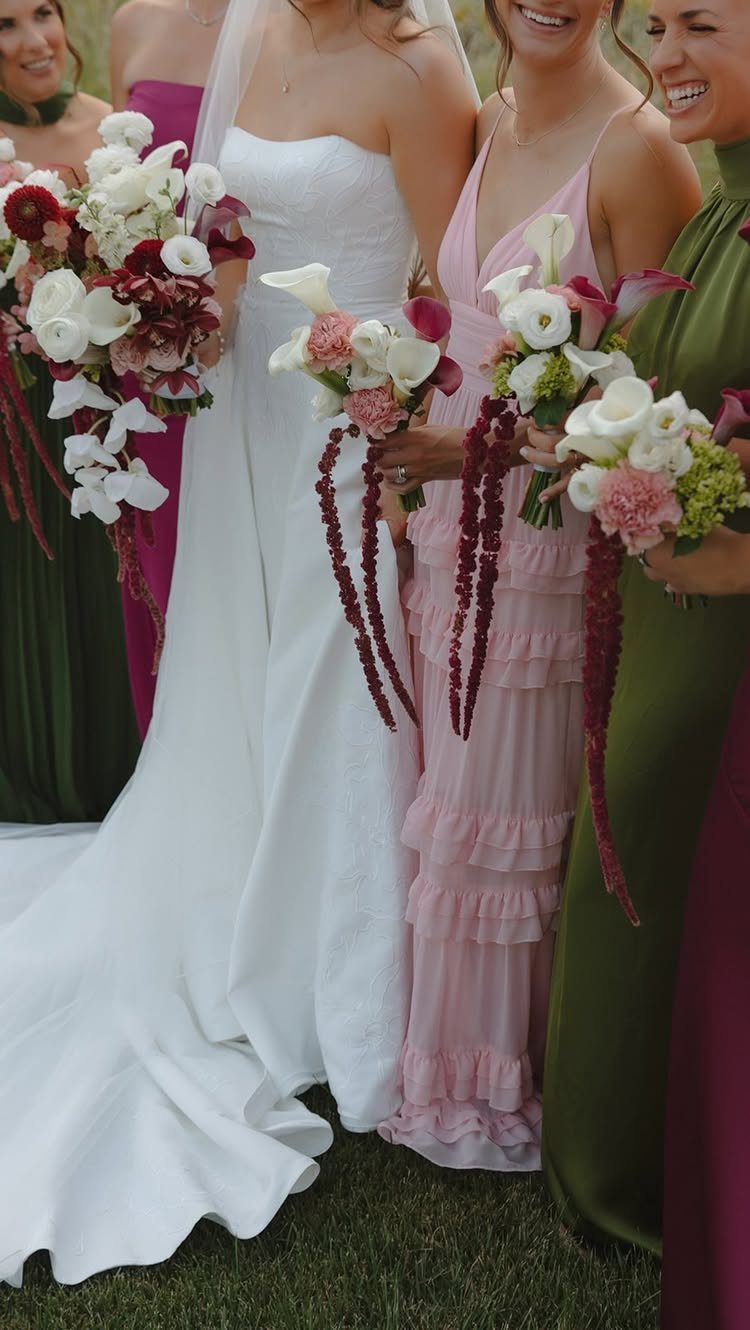 Bride and bridesmaids in white, olive, pink, and magenta dresses holding floral bouquets.