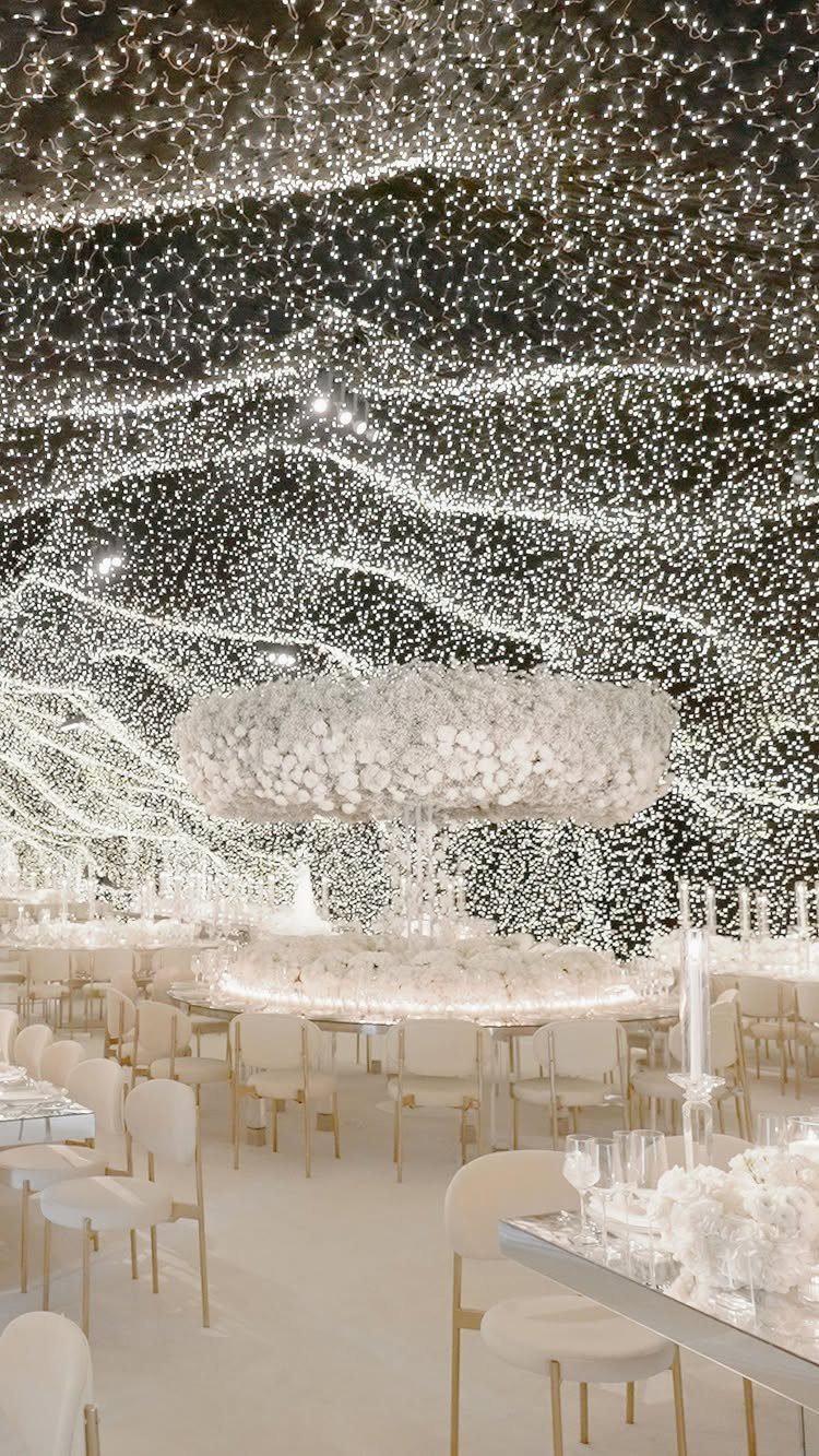 Starry fairy light ceiling over white wedding tables with large floral centerpieces