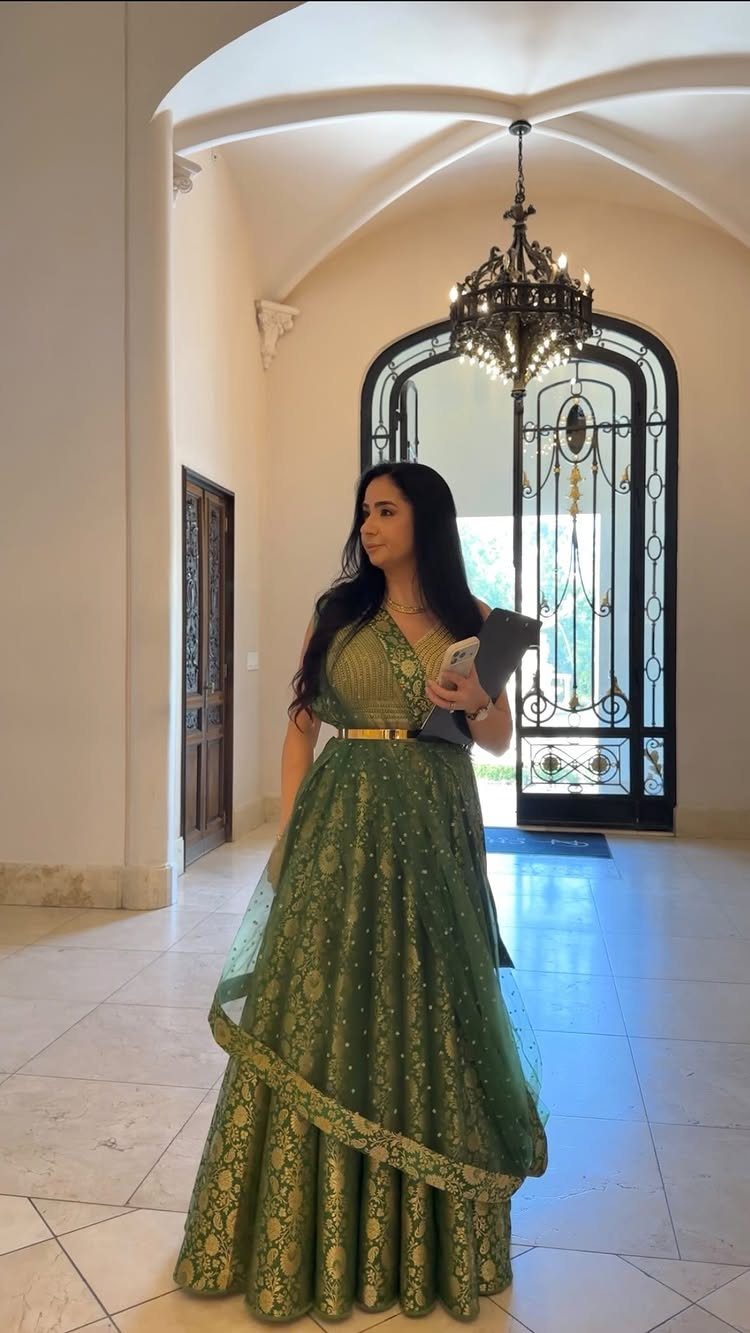 Woman in a green embroidered gown holding a folder in a bright hallway