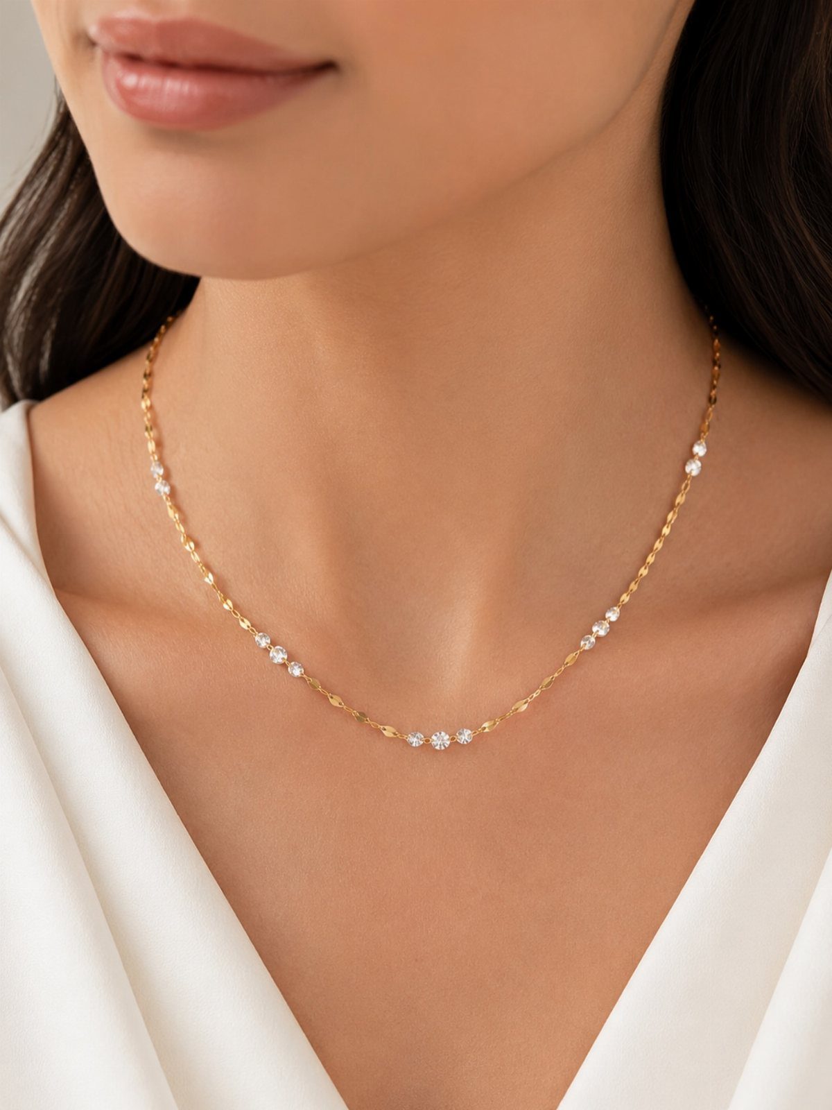 Gold chain necklace with small sparkling diamonds worn on a white V-neck top
