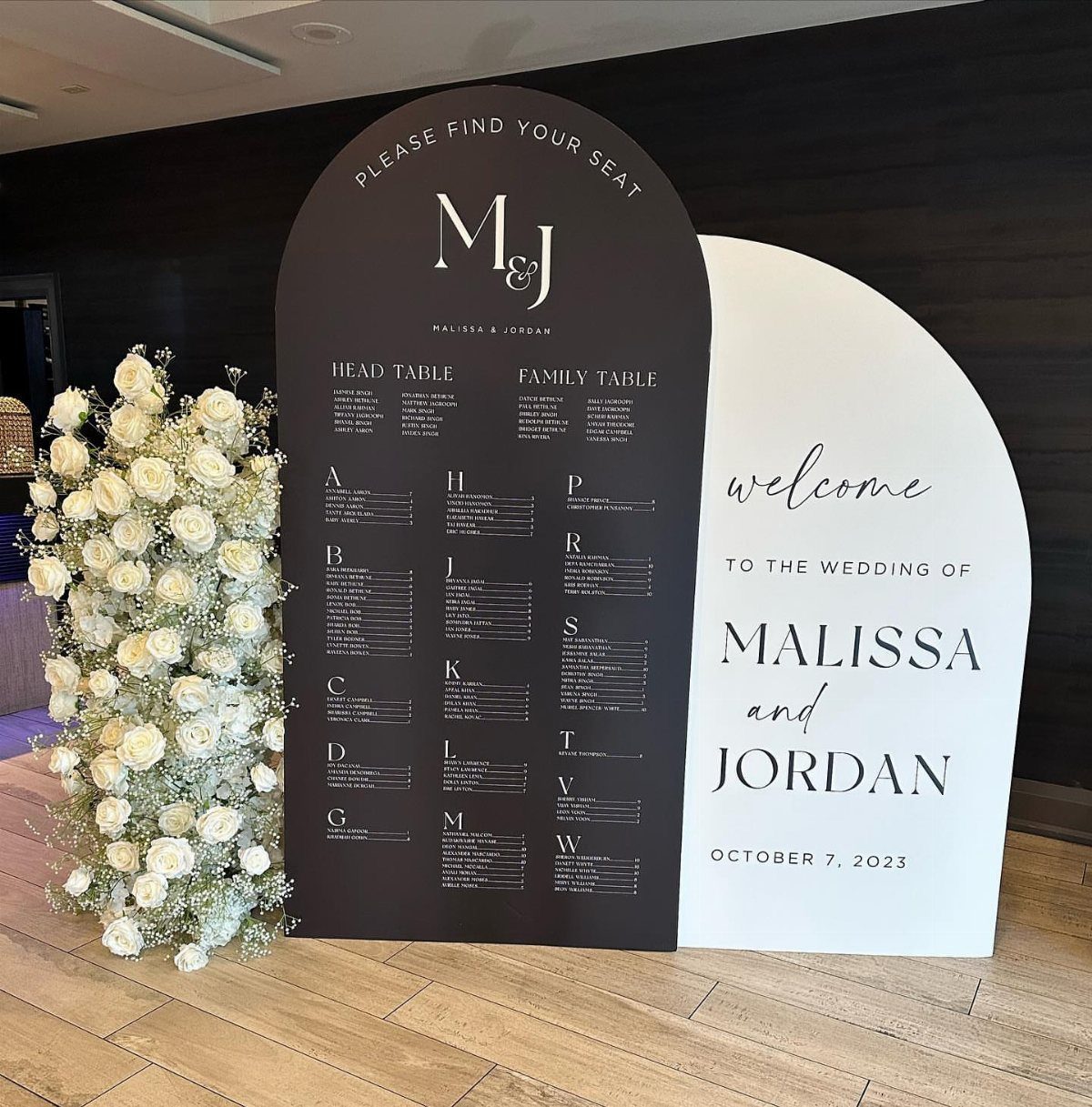 Wedding seating chart and welcome sign with white floral arrangement on wooden floor