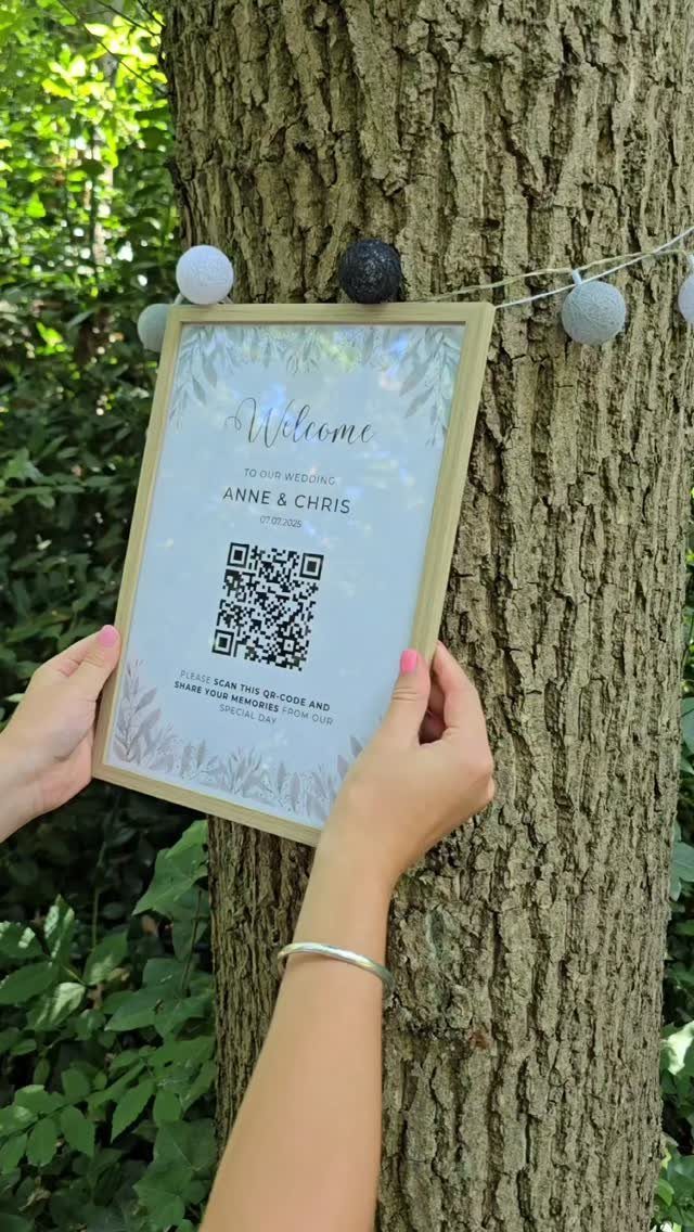 Framed wedding welcome sign with QR code held against a textured tree trunk.