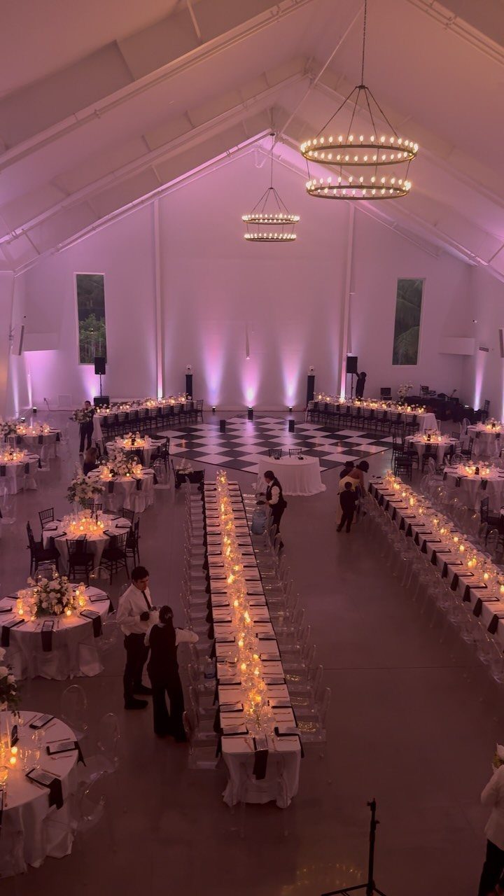 Wedding reception hall with purple uplighting, warm candlelight, and large circular chandeliers.