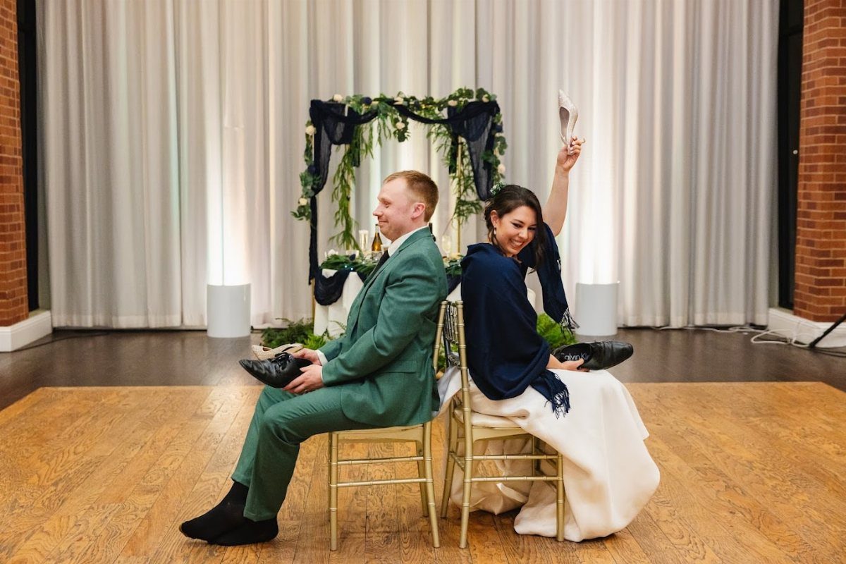 Bride and groom sitting back-to-back playing the shoe game at a wedding reception.