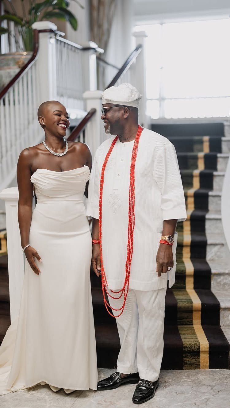 Smiling couple in white wedding attire standing together on a staircase.