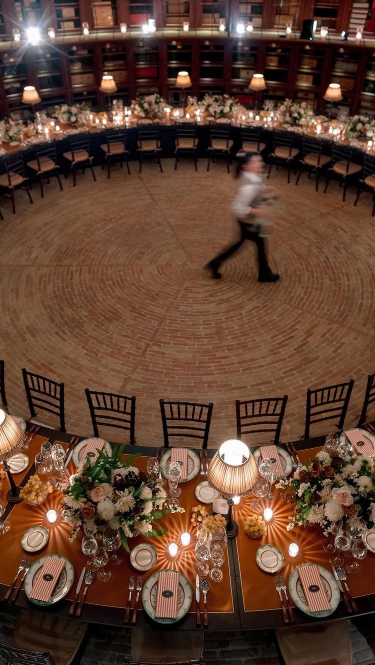 Circular dining tables with floral centerpieces inside a grand, dark wood library venue.