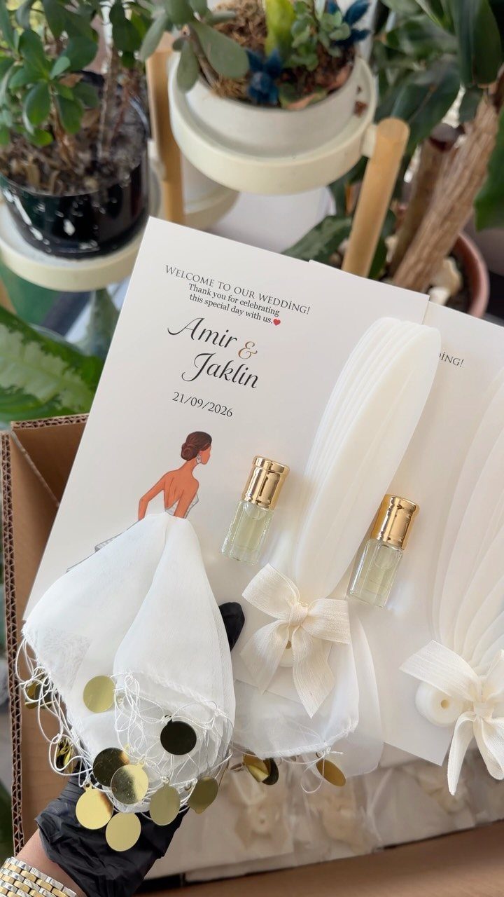 Small perfume bottles and white fabric pouches as wedding favors on personalized cards.