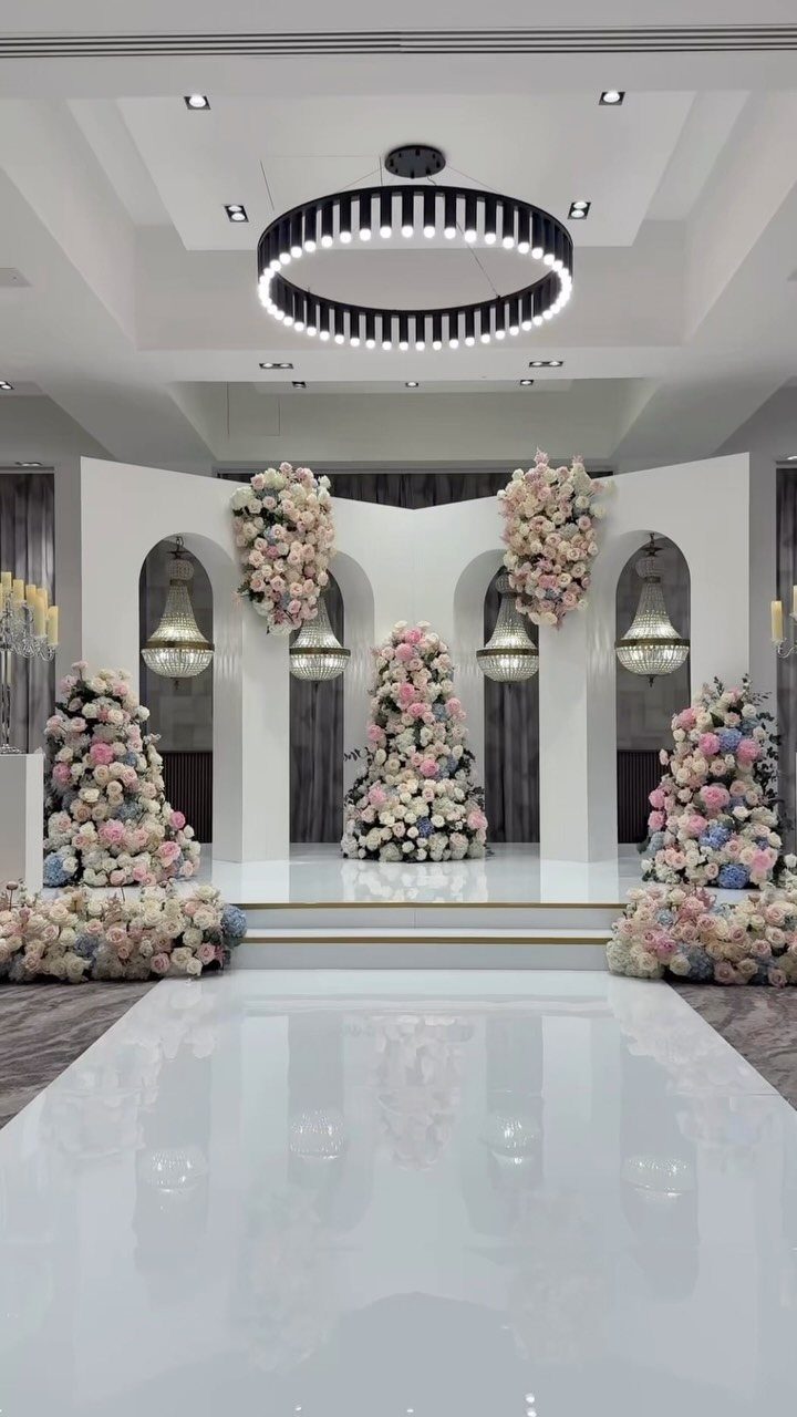 White wedding venue with glossy dance floor and large pink and white floral arrangements.