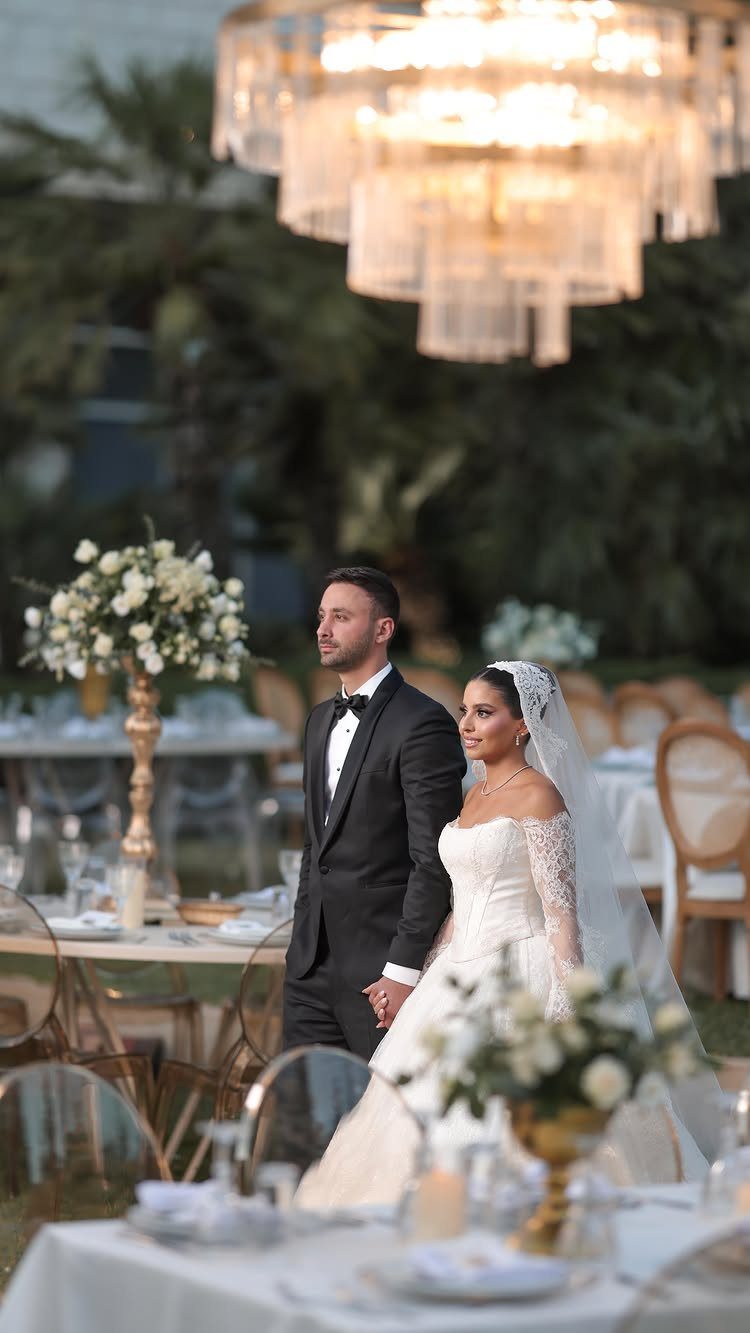 Bride and groom holding hands at an outdoor wedding reception with white flowers.
