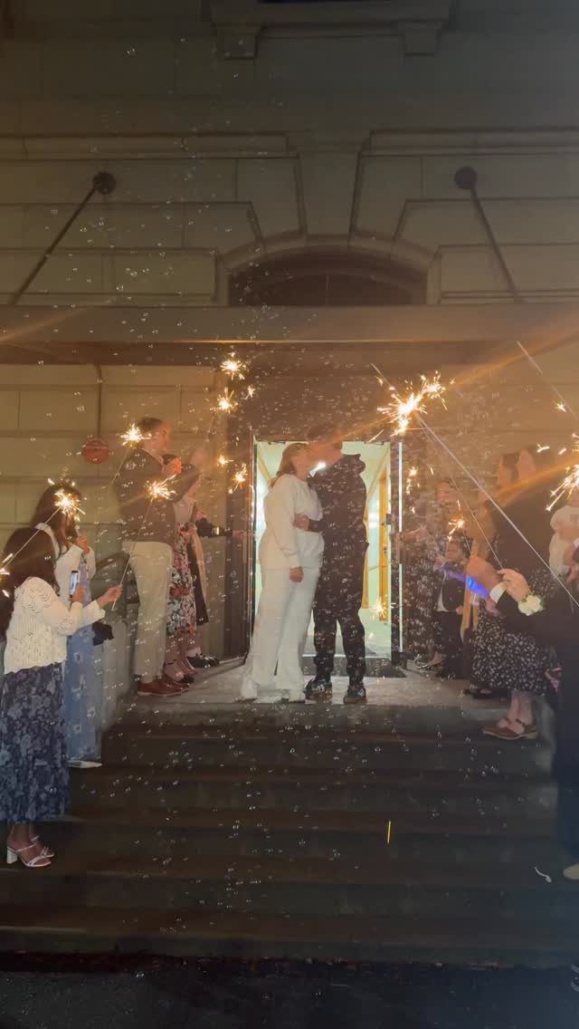 Couple kissing on steps surrounded by guests holding glowing sparklers at night