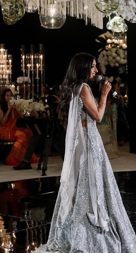 Woman in a silver gown speaking into a microphone at a wedding reception.
