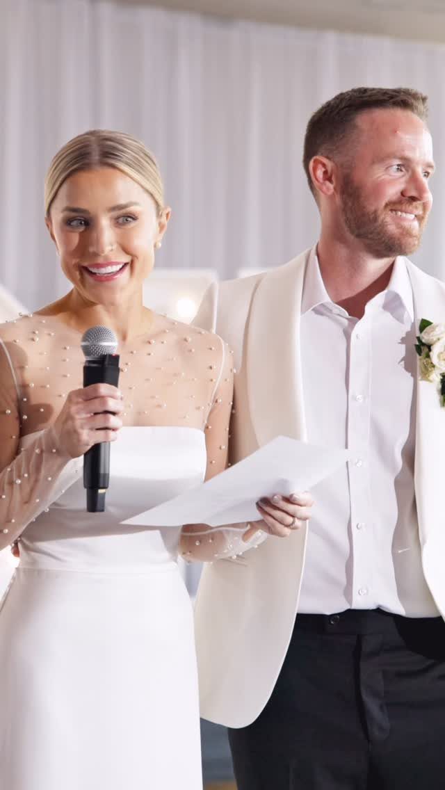 Bride speaking into a microphone while holding notes next to the groom.