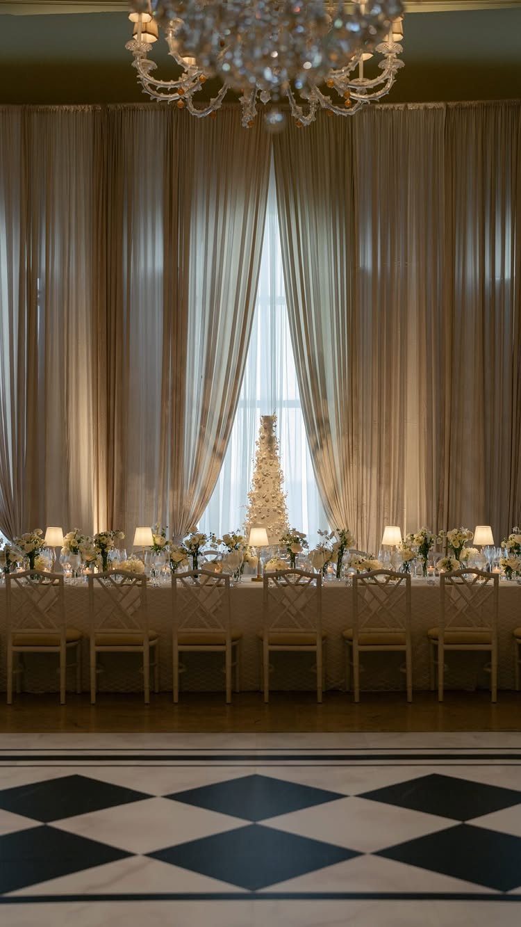 Elegant ballroom reception setup with a long decorated table and crystal chandelier.