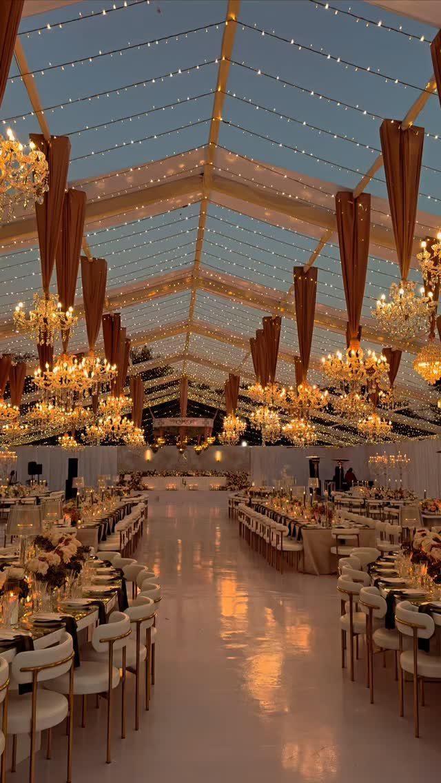 Luxurious wedding reception venue inside a transparent tent with chandeliers and long tables.