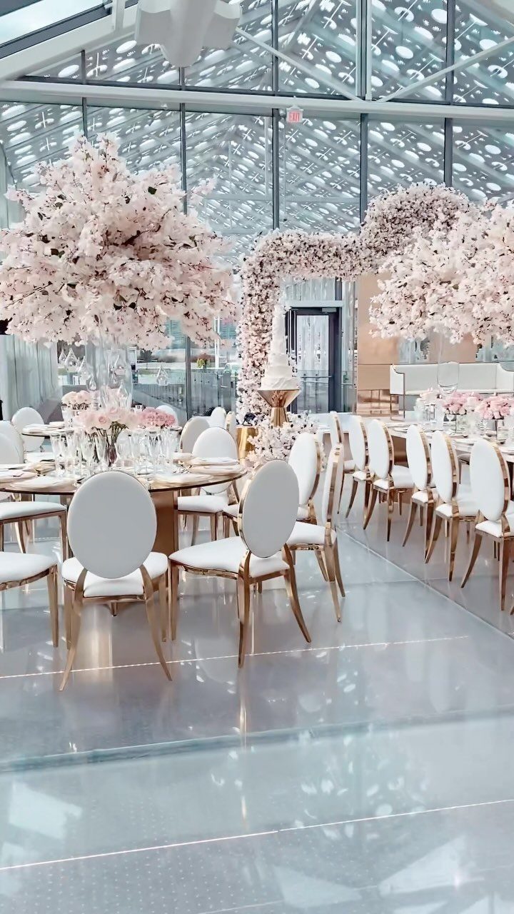 Modern event space with glass walls, white chairs, and pink cherry blossom centerpieces.