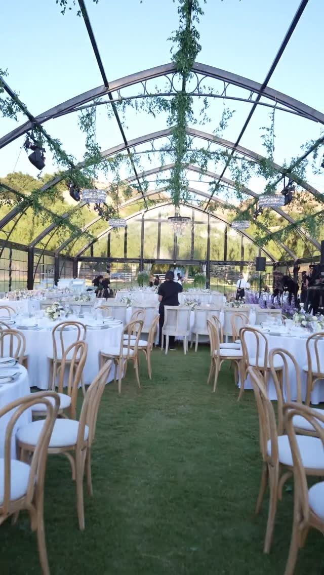Wedding reception tables under a transparent glass marquee on a green grass lawn