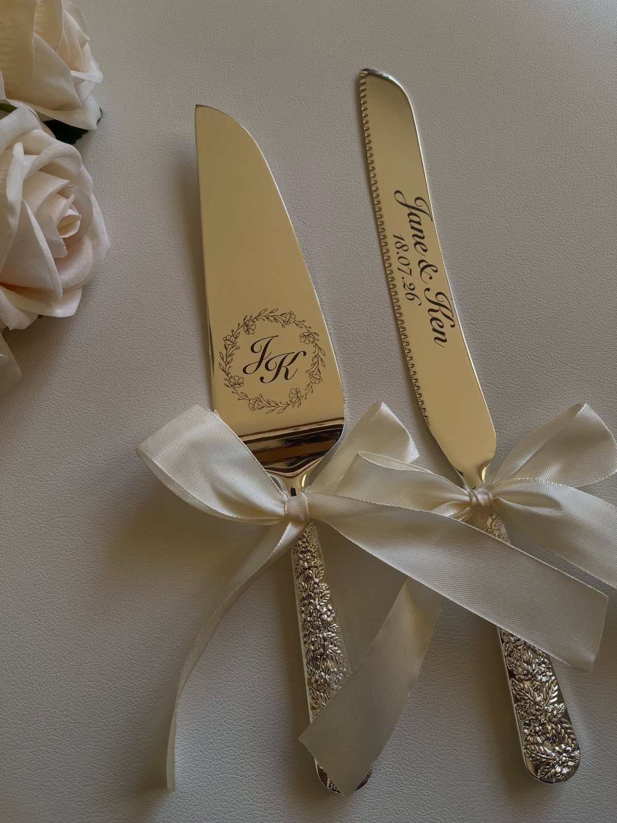 Engraved silver cake server and knife tied with a white satin ribbon.