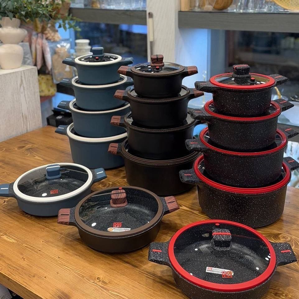 Stacks of colorful ceramic pots and pans with lids on a wooden table.