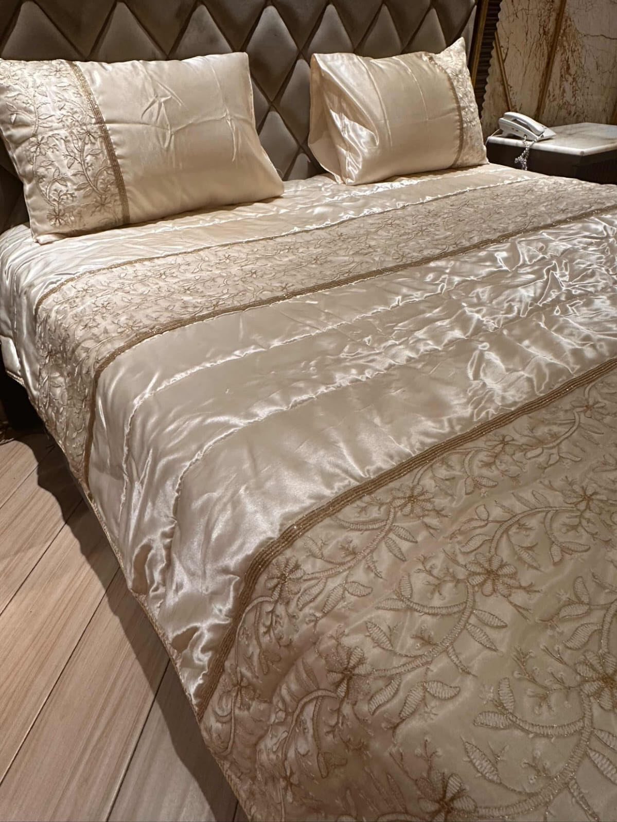 Champagne satin bedding with floral embroidery on a bed with quilted headboard