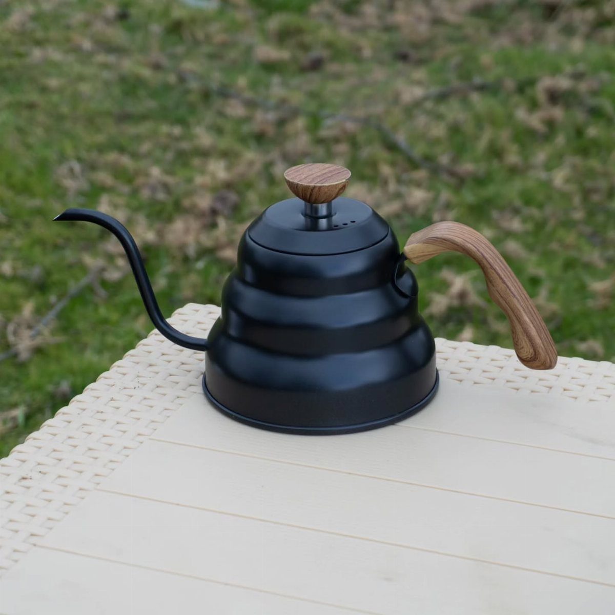 Matte black gooseneck kettle with wooden accents on a light wooden table outdoors