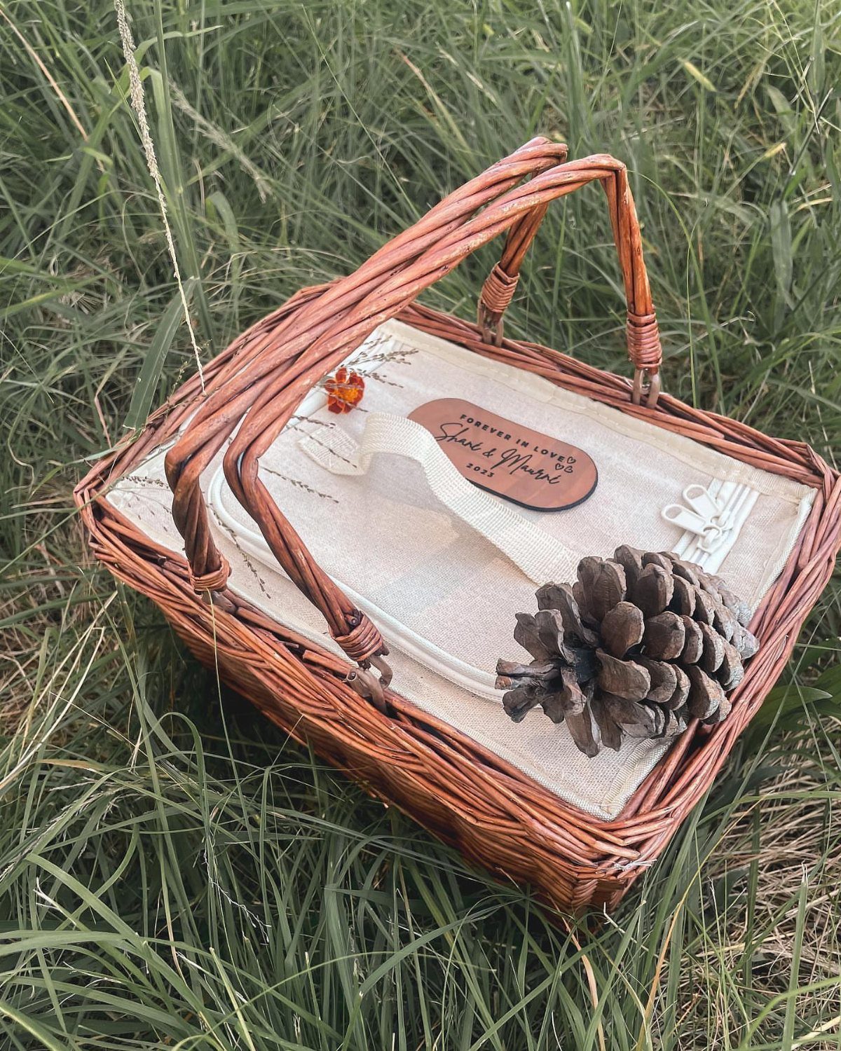 Woven wicker picnic basket with a white liner and pinecone in green grass