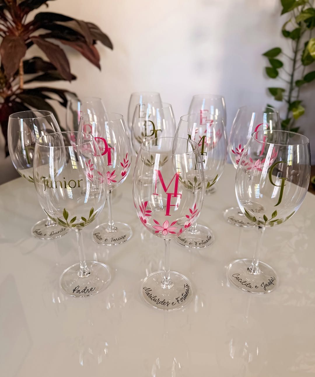 Personalized wine glasses with pink floral designs and engraved names on a white surface.