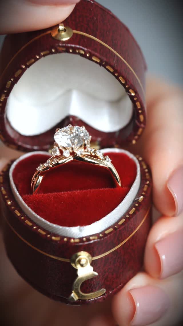 Gold diamond ring in a heart-shaped red velvet jewelry box held by a hand.