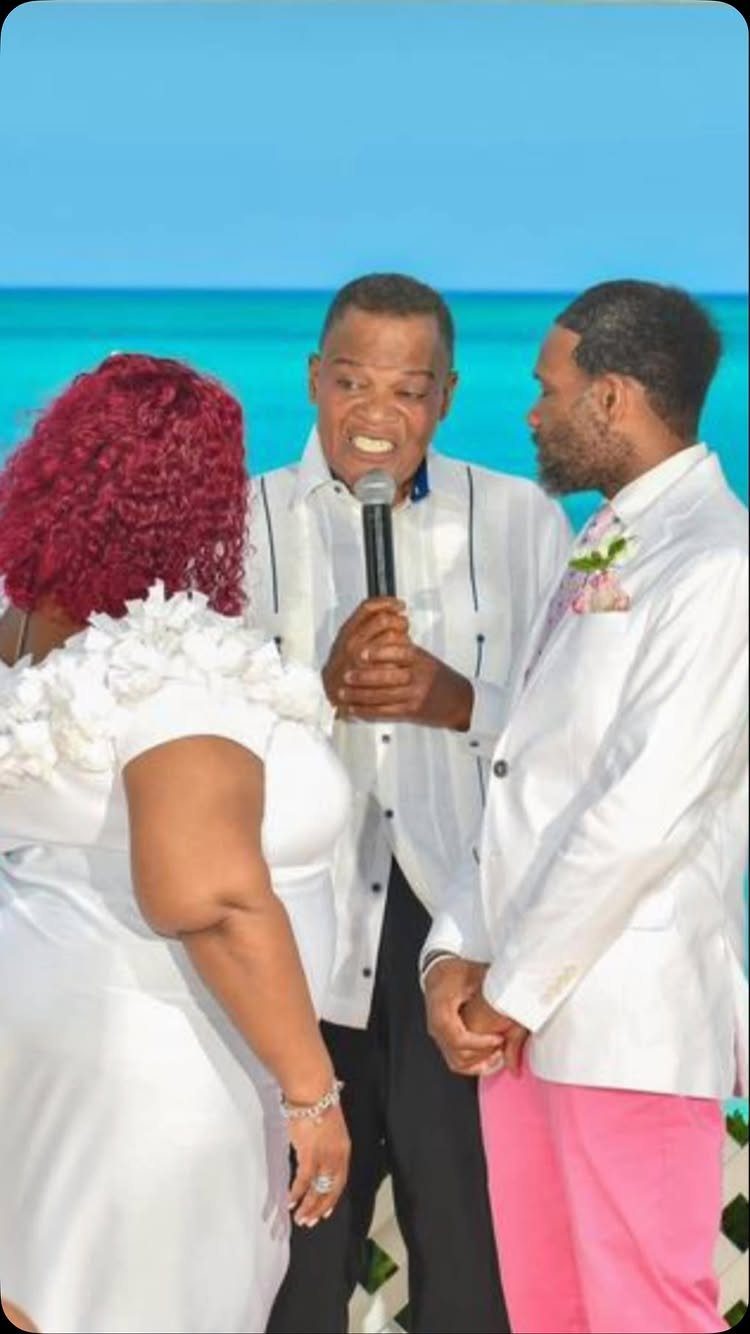Couple holding hands during a ceremony on a beach with an officiant speaking.