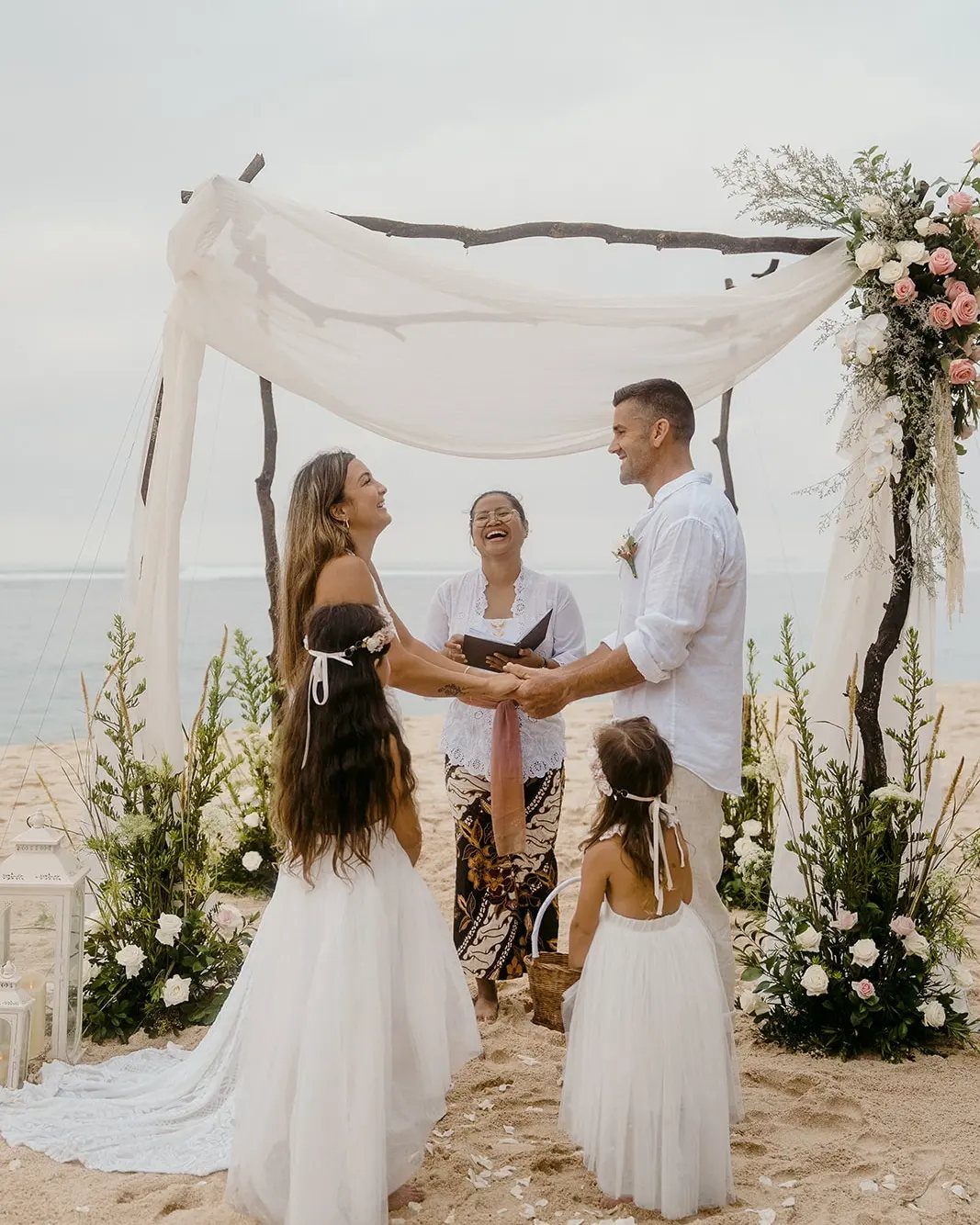 Couple and two young girls in white dresses during a beach wedding ceremony.