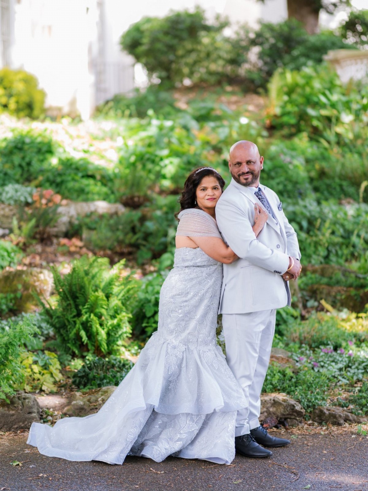 Couple in formal light blue and grey attire posing in a lush garden.