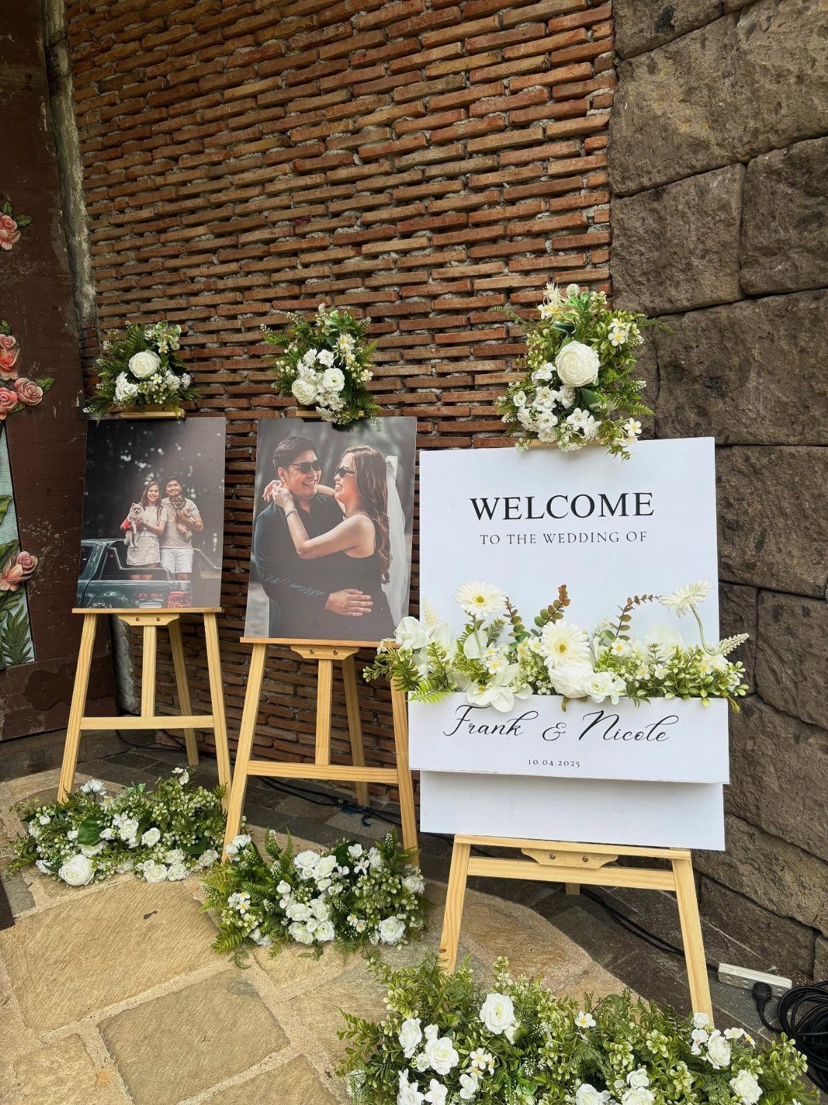 Wedding welcome sign and couple portraits on wooden easels with white floral arrangements.
