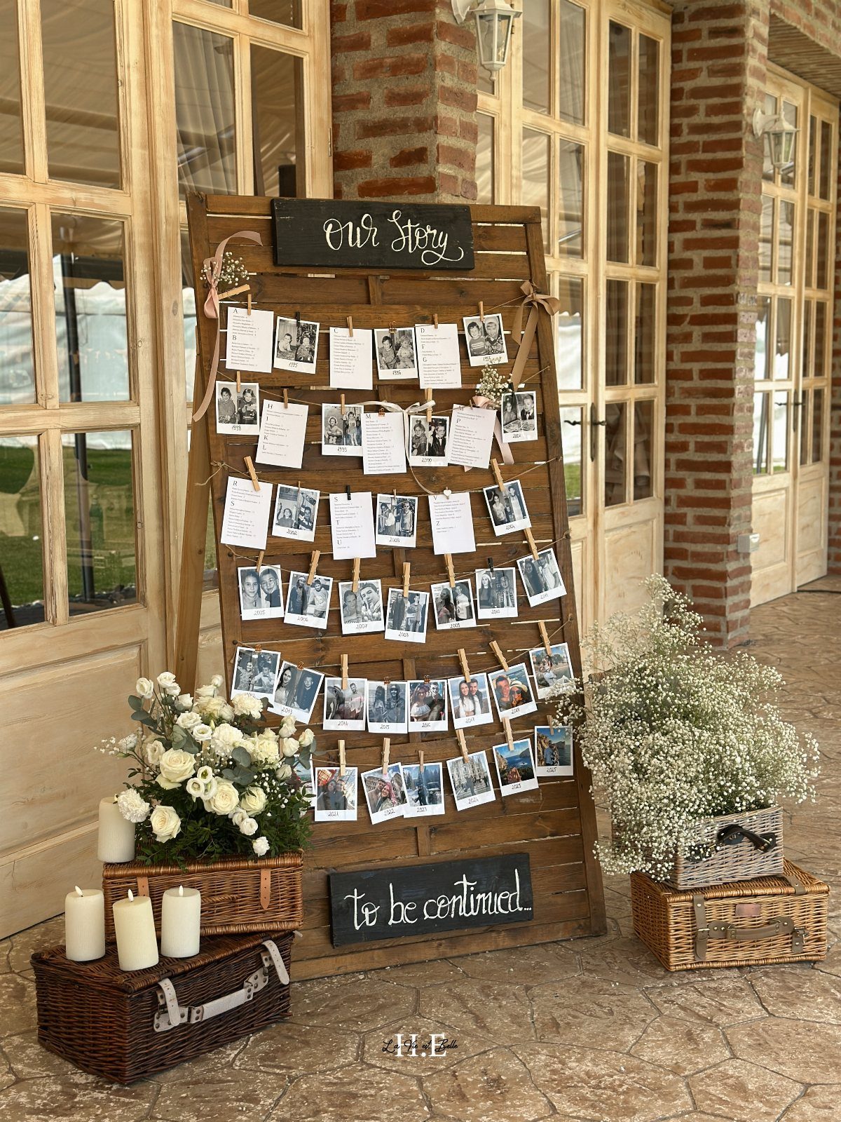 Wooden memory board with clipped photos, chalkboards, and white floral arrangements on stone.