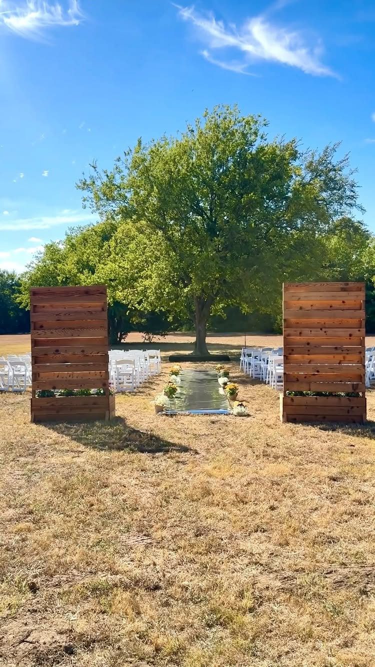 Rustic outdoor ceremony setup with wooden walls, white aisle runner, and white chairs.