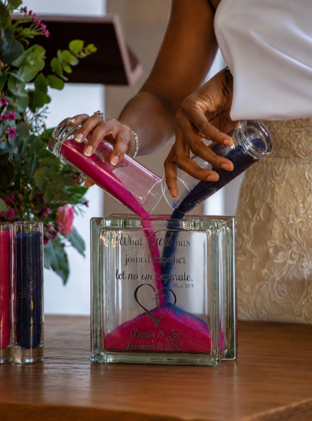 Two people pouring pink and blue sand into a glass unity vessel.